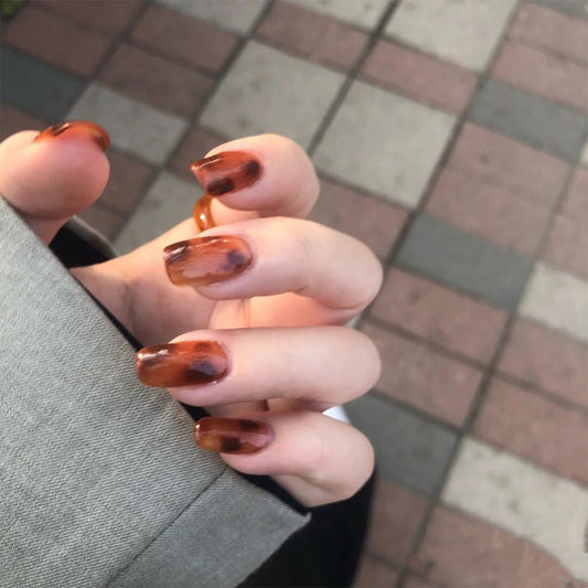 A hand with press-on nails featuring a long almond brown design.