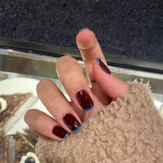A hand with false nails painted in brown with blue tips, pressing onto the fingers.