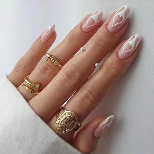 A hand with long oval nails with white flame designs, wearing gold rings.