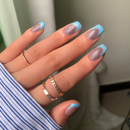 A hand with short square nails with a French tip design, featuring gray at the base transitioning to blue at the tips.