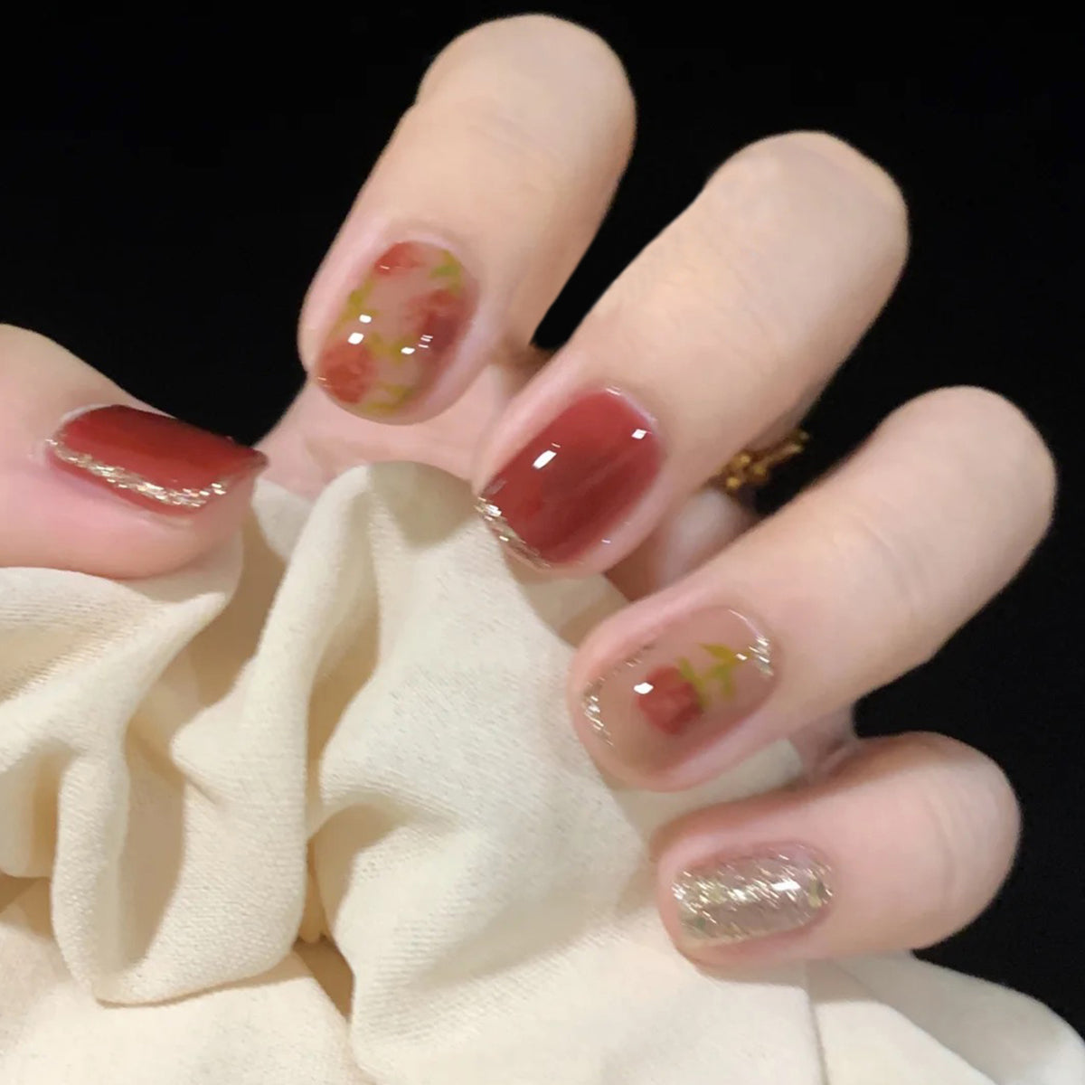 A hand with short square red glitter press on nails, some with rose patterns.