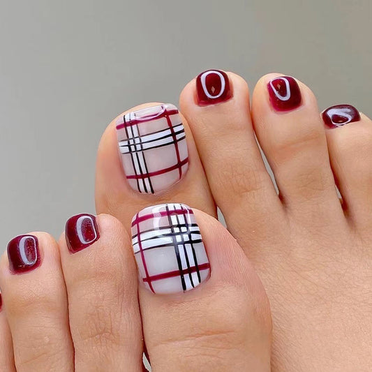 Toes with red and white plaid nail design on a neutral background