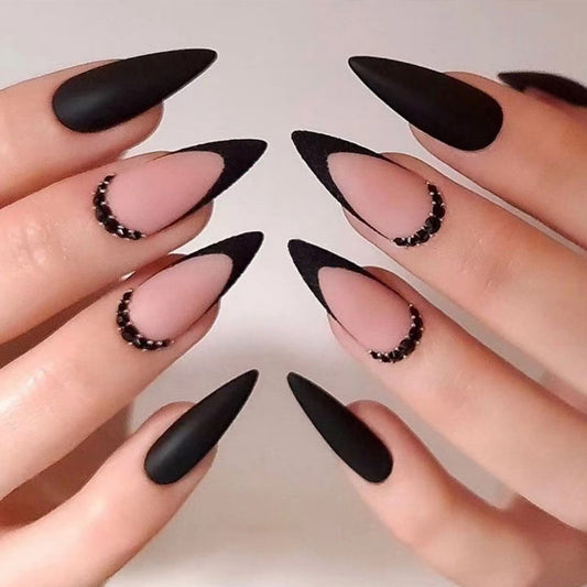 A set of long almond-shaped false nails in black, adorned with small pearl embellishments.