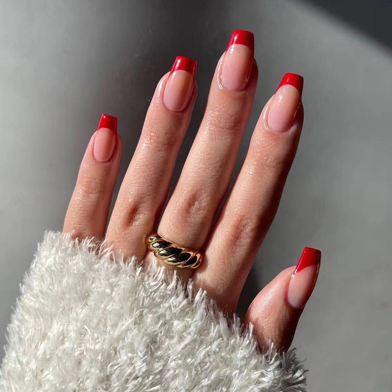 A hand with press-on nails featuring a medium coffin shape with red French tips.