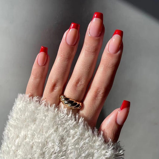 A hand with press-on nails featuring a medium coffin shape with red French tips.