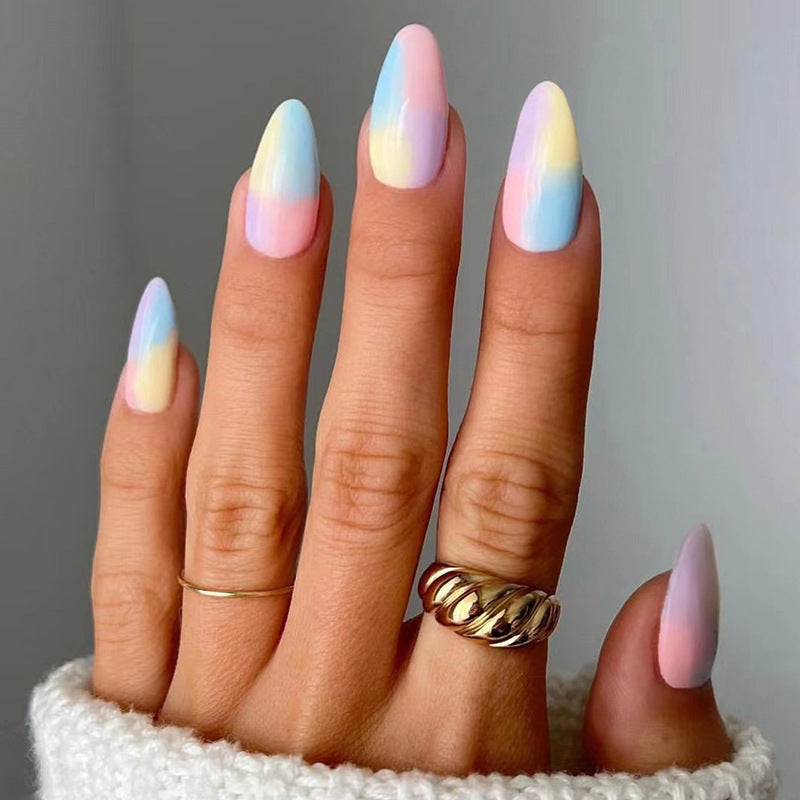 A person's hand with medium almond pastel ombre press on nails featuring an iridescent glow, shown holding rings.