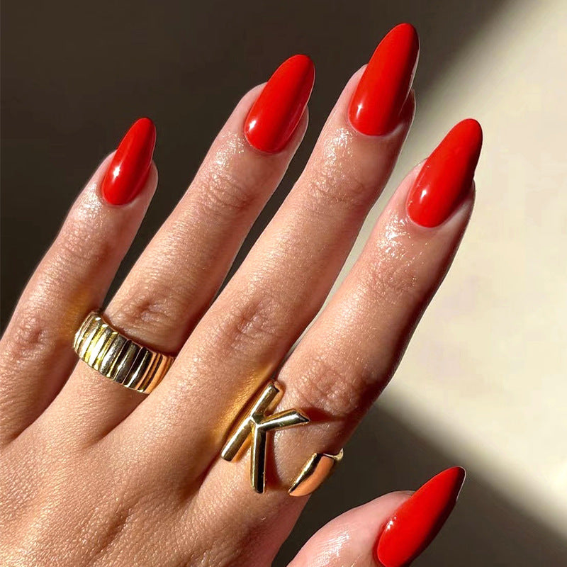 A close-up image of a person's hand showcasing long almond-shaped red press-on nails with a glossy finish.