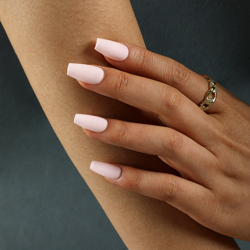 Close-up of a hand with pink nails and a gold ring on a dark background