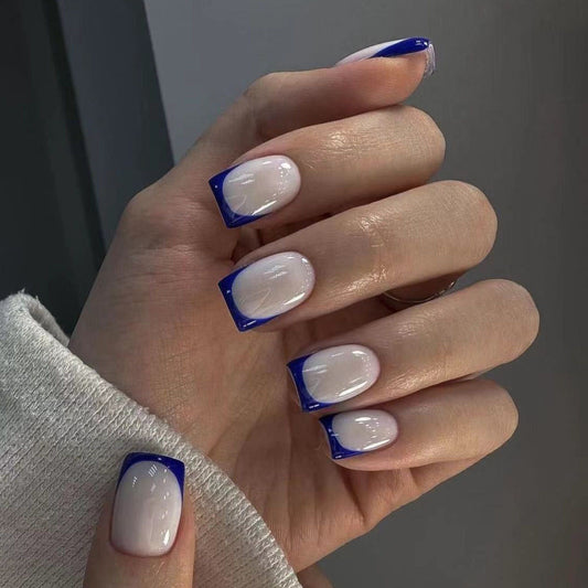 A hand showcasing press-on nails with a white base and blue tips, representing a French tip style.