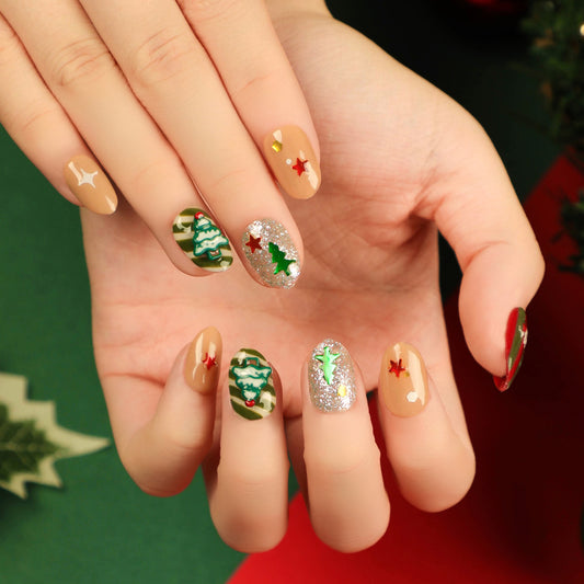 A hand with press-on nails featuring a Christmas tree and star designs in green, white, and red colors, indicative of the holiday season.