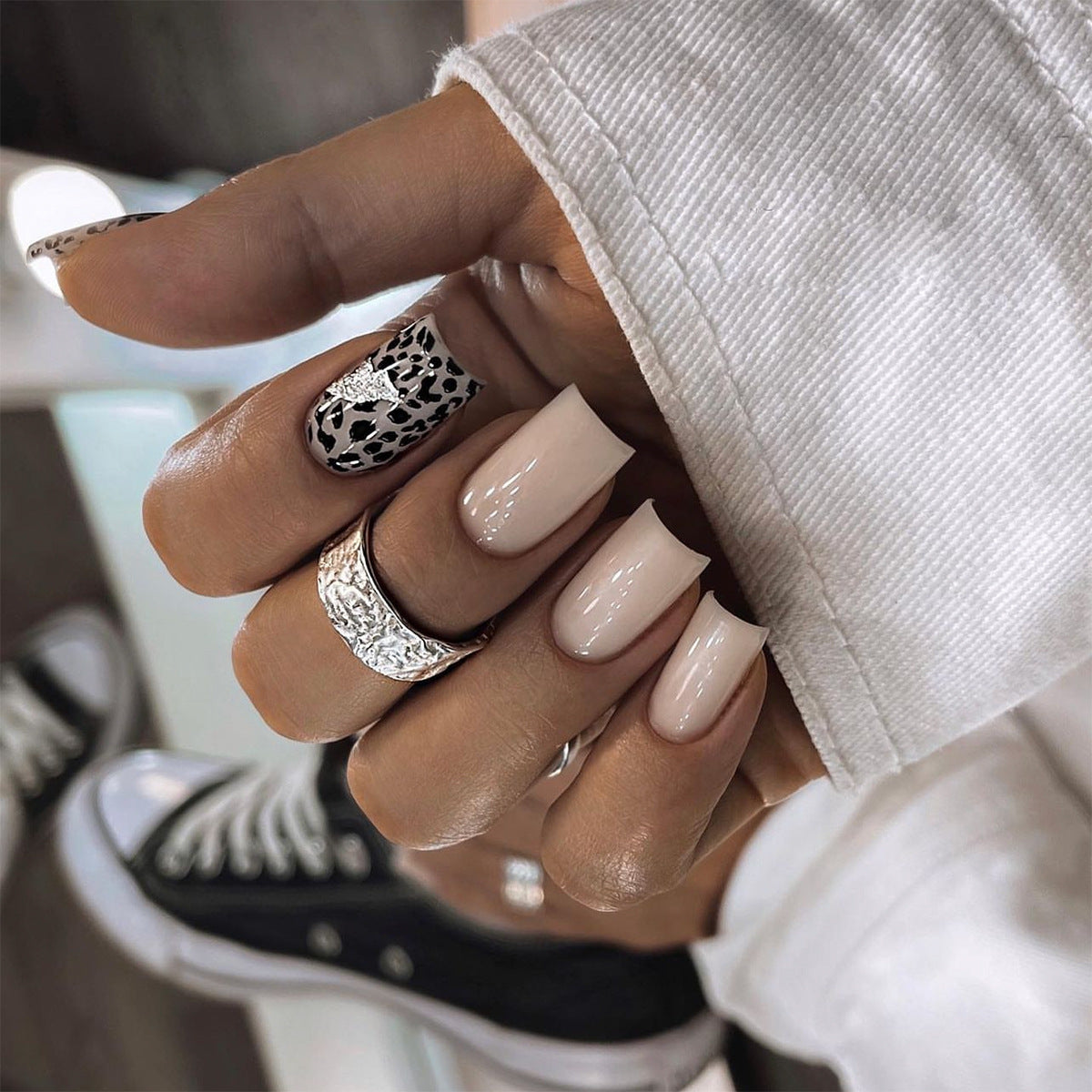 Hand with beige nail polish and decorative rings, blurred background