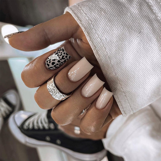 Hand with beige nail polish and decorative rings, blurred background