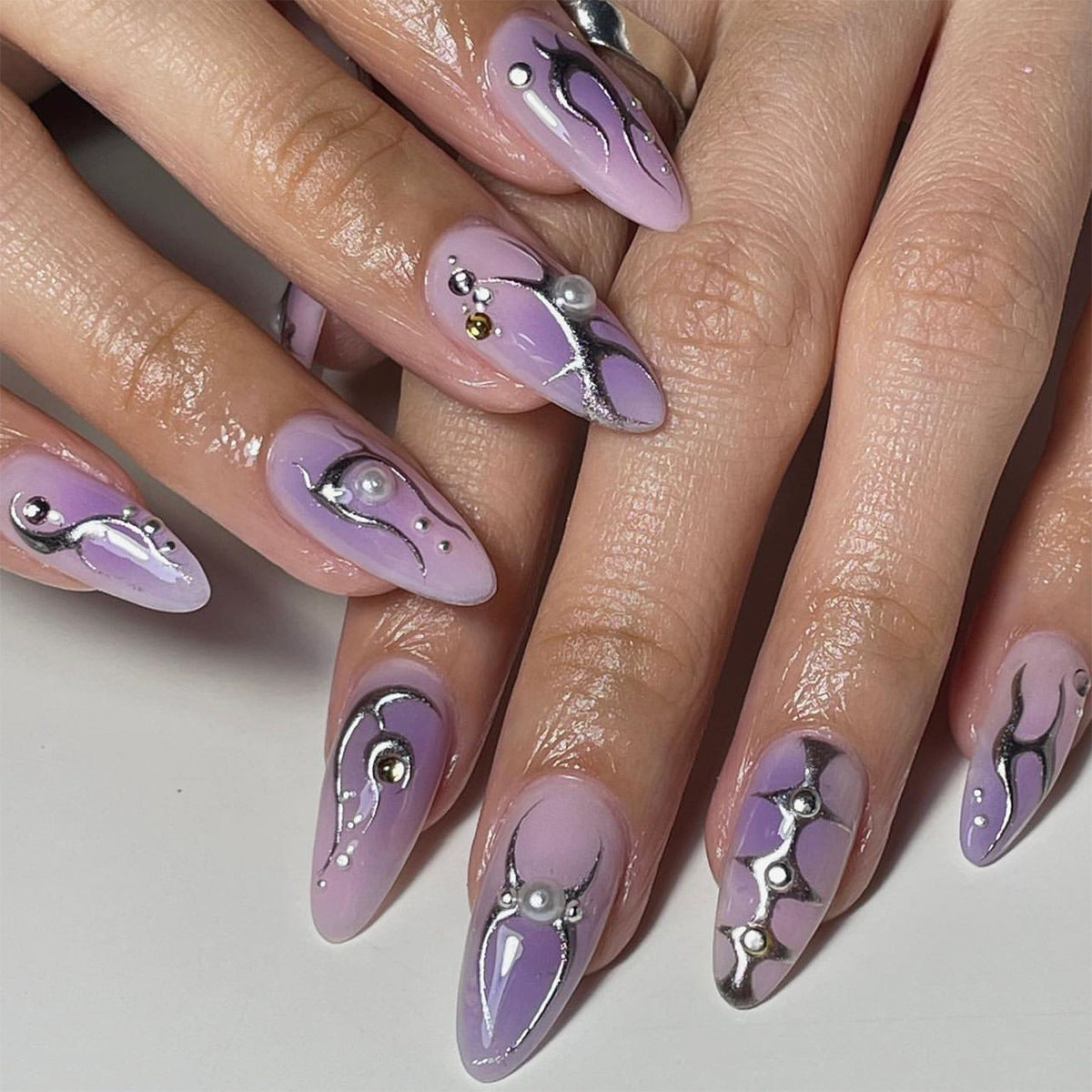 A set of press-on nails featuring a medium almond shape in a purple color with decorative patterns.
