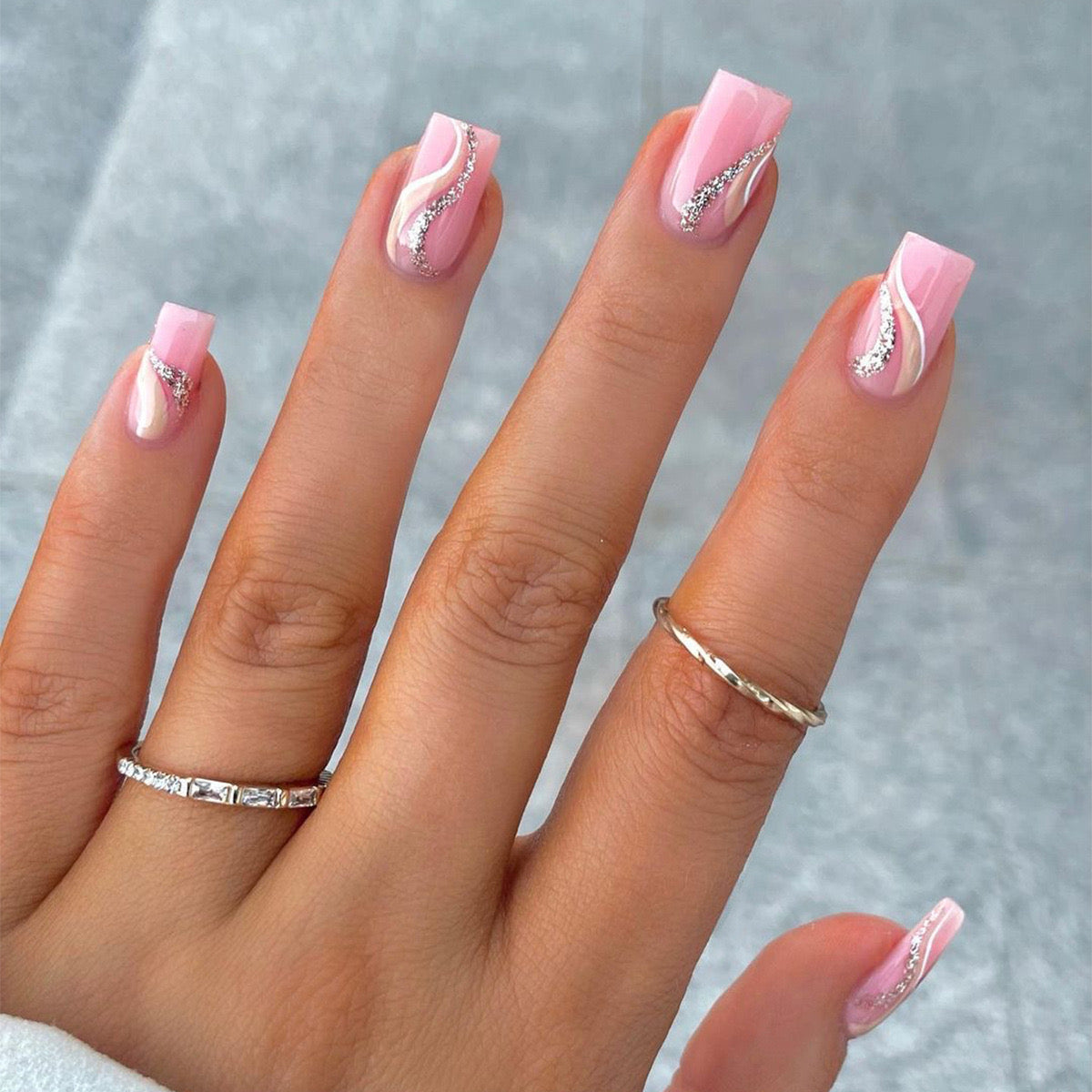 Hand with pink nails and silver decorations on a neutral background
