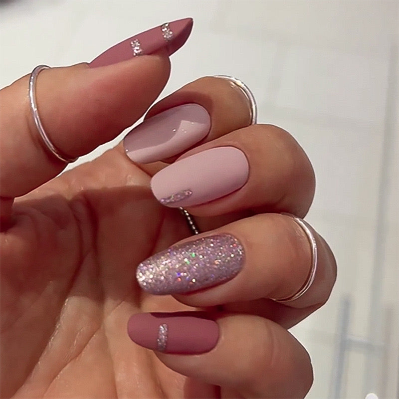 Close-up of a hand with pink and glittery nails against a neutral background