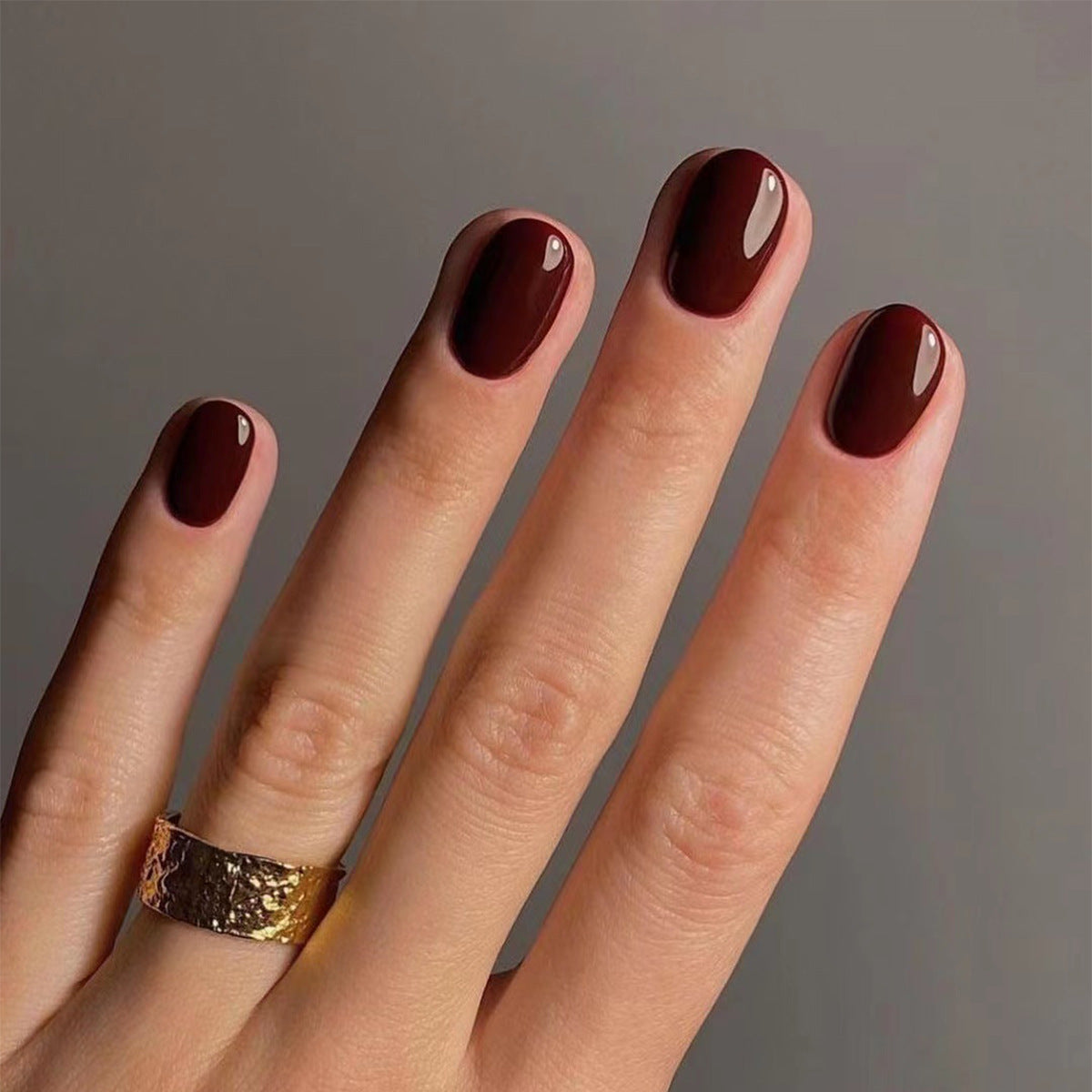 Hand with dark red nail polish on a plain background