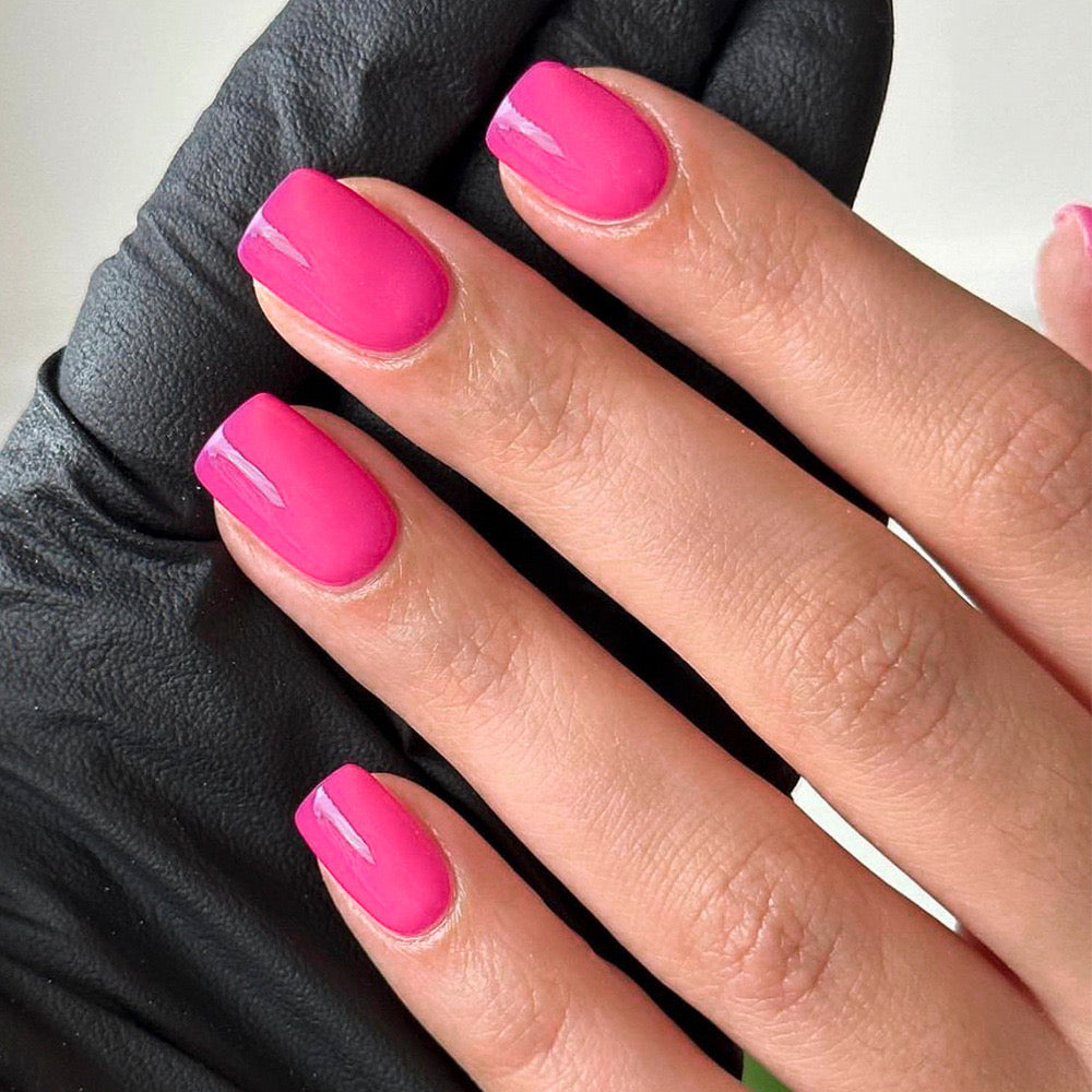 A close-up image of a hand with press-on nails painted in a vibrant fuchsia color, indicating a square, short nail style.