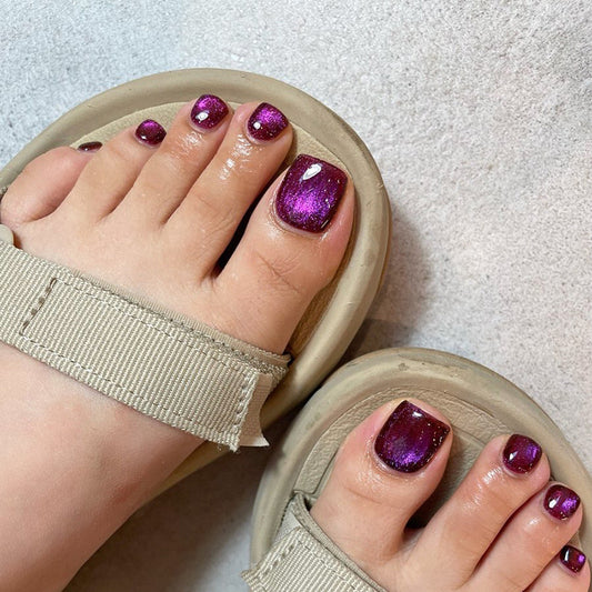 A pair of feet wearing sandals with deep purple glittery nail polish.