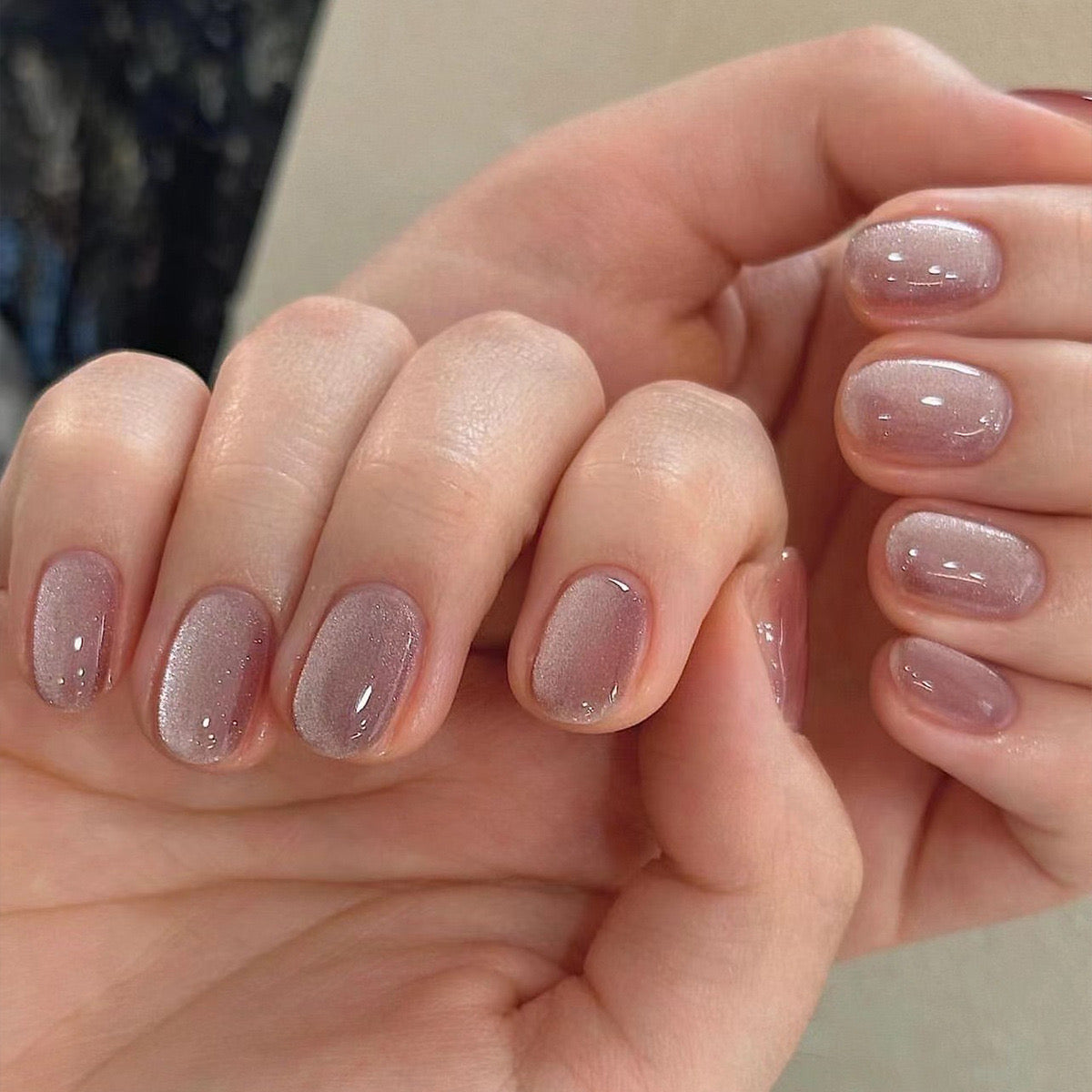 A pair of mauve press-on nails with subtle glitter, displayed on a hand.