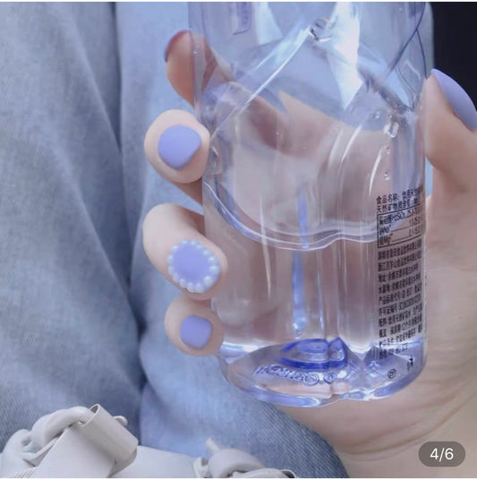 A person's hand holding a water bottle, with short oval purple matte press-on nails.