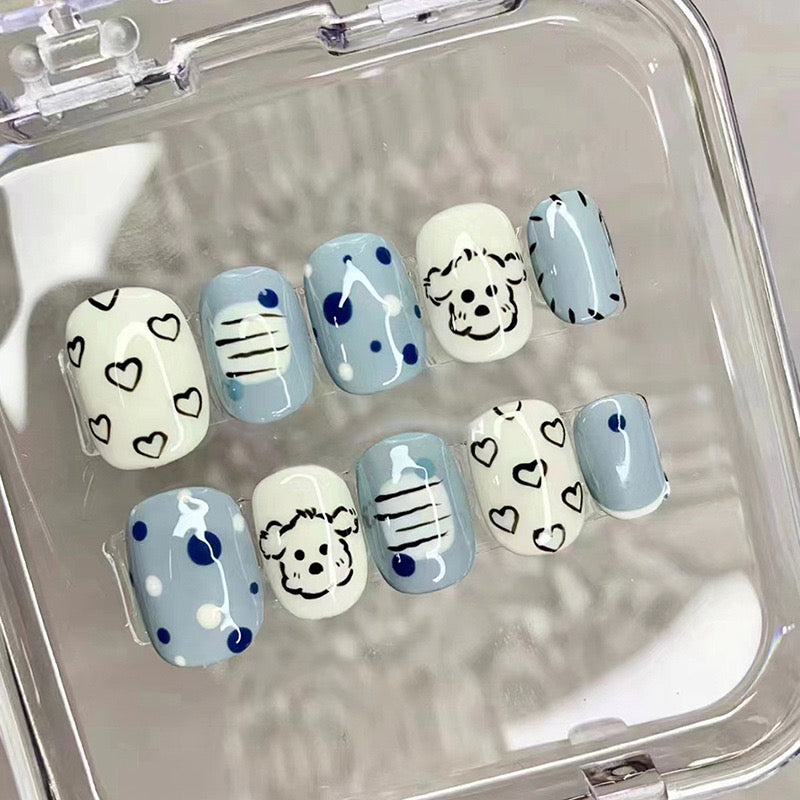 A set of short squoval blue press-on nails with cartoon puppy dog designs and heart patterns.
