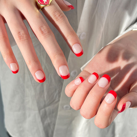 Close-up of hands with red and white nail polish on a neutral background