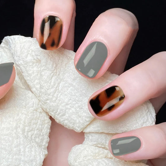 A person's fingers showcasing press-on nails with a blue leopard print design, with a square, short nail shape.