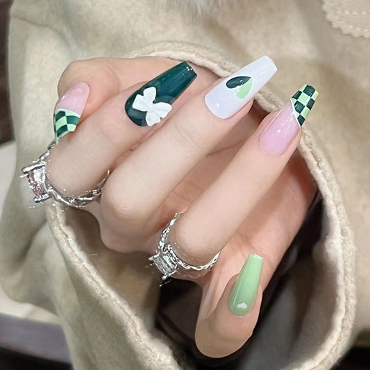 A hand with long green fingernails featuring a green hearts pattern and a pink tip.