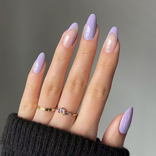 Hand with lavender and nude nail polish wearing a gold ring on a gray background