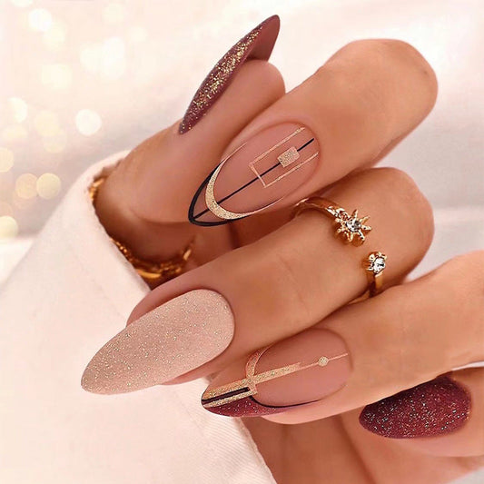 A set of press-on nails featuring long almond shapes with a gold glitter design.