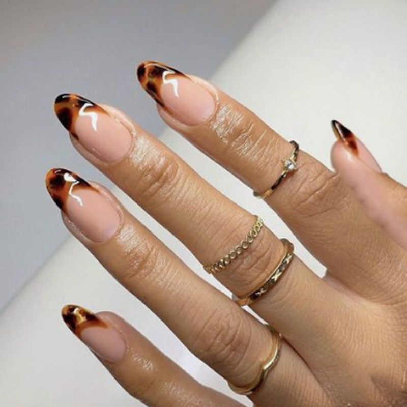 Hand with tortoiseshell nail design and gold rings on a neutral background