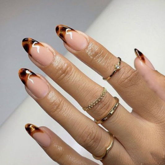 Hand with tortoiseshell nail design and gold rings on a neutral background