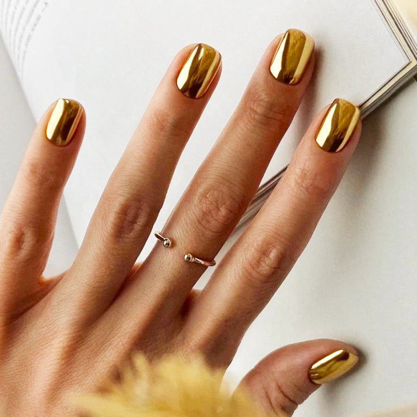 A person's hand with gold-colored, oval-shaped press-on nails, displayed with a book in the background.