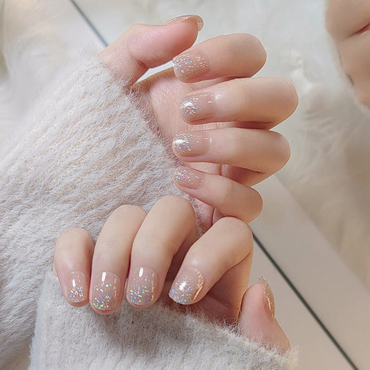 A pair of hands with short oval-shaped nails with a silver glitter design.