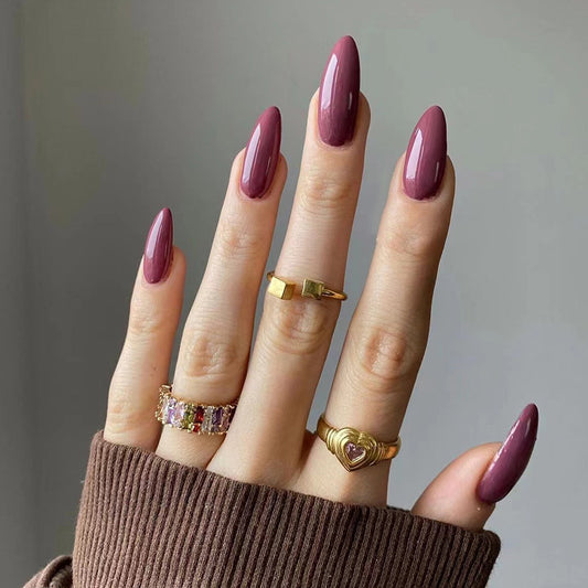 Hand with burgundy nails and gold rings on a neutral background