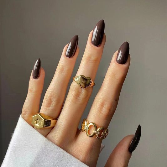 Hand with dark nail polish wearing gold rings on a neutral background