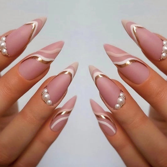 A set of long almond-shaped pink nails with white and gold geometric patterns and pearls.