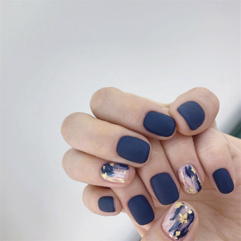 Hand with dark blue nail polish and gold flake accents on a light gray background