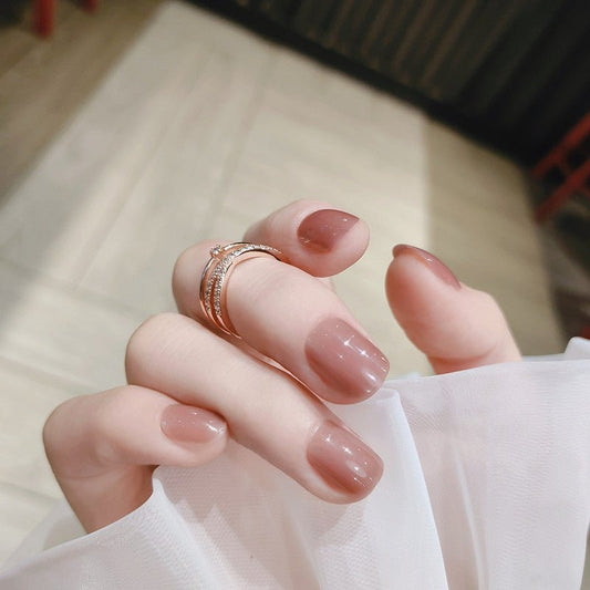 A person's hand with short, square-shaped pink nails, wearing a ring, and partially covered by a white fabric.