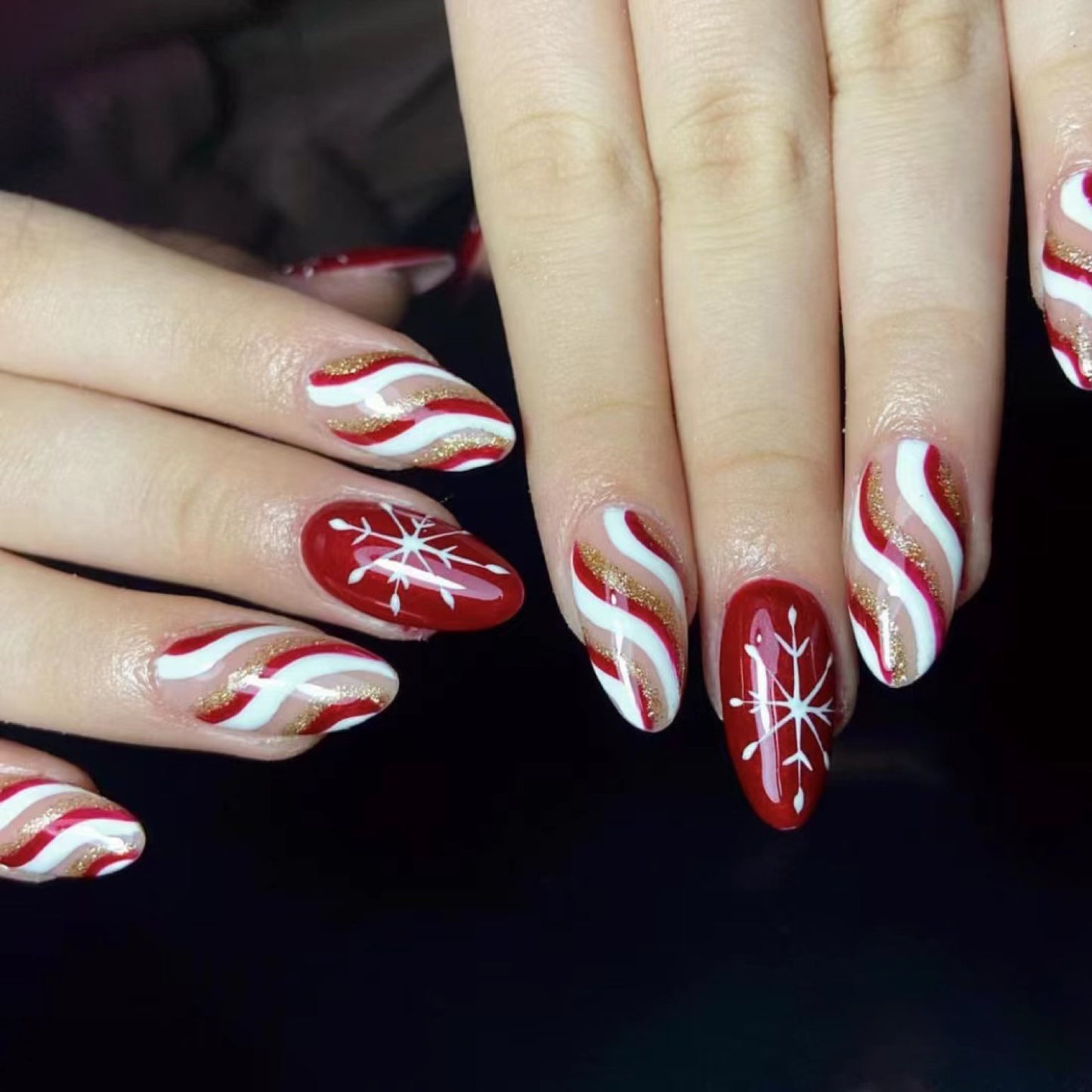 A photo showing a set of press-on nails with a red base and white and gold holiday-themed designs, including snowflakes.