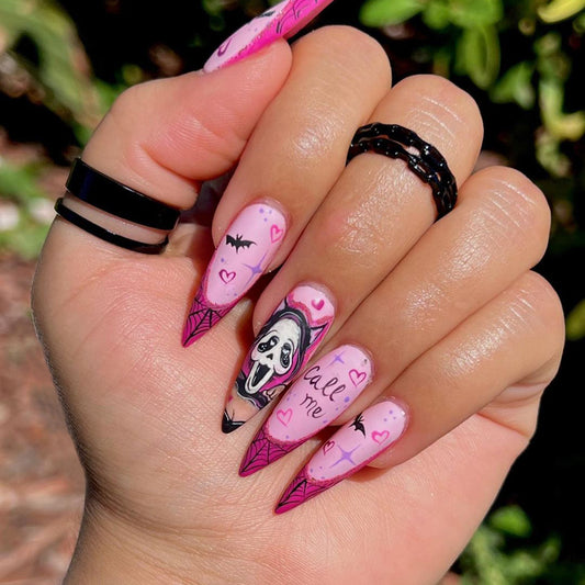 A hand with pink press-on nails featuring a Halloween design with a character and decorative elements.