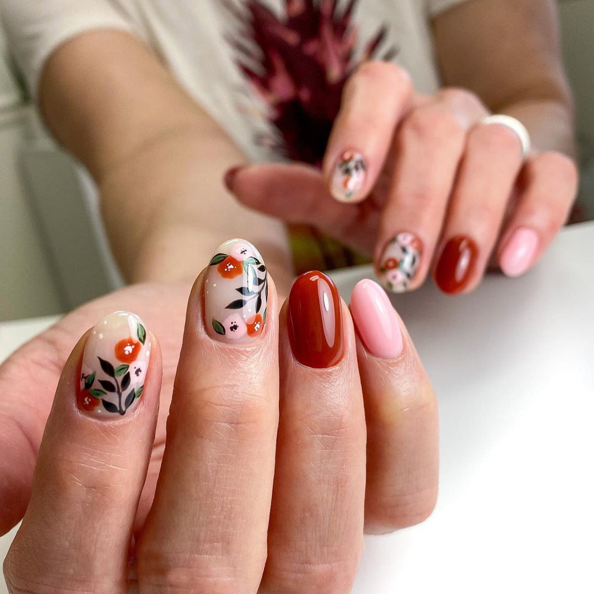 A person's hands displaying press-on nails with a red fall theme, including floral patterns and a variety of shades of red.