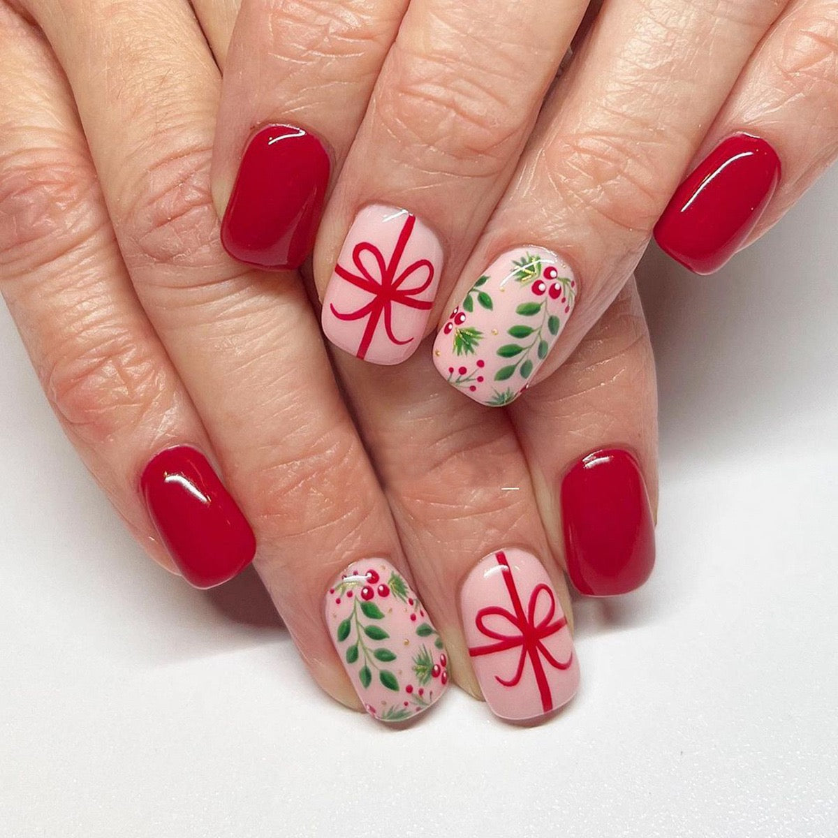 Close-up of a hand with red and festive nail art on a white background