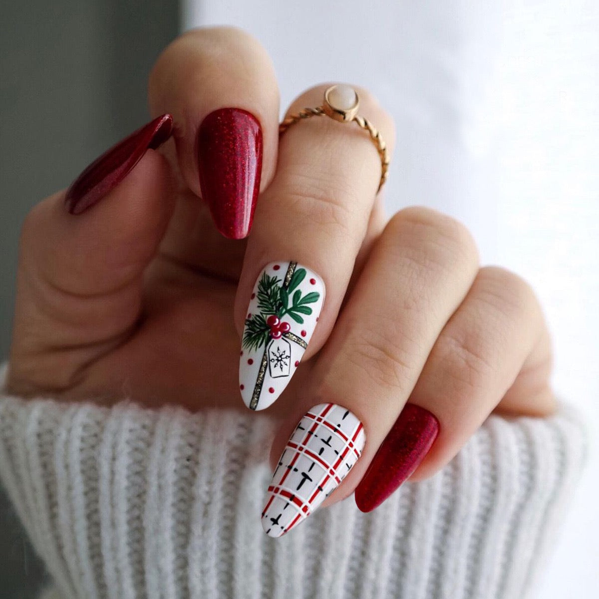 A set of long, almond-shaped, white holiday press-on nails with red accents and a holly design.