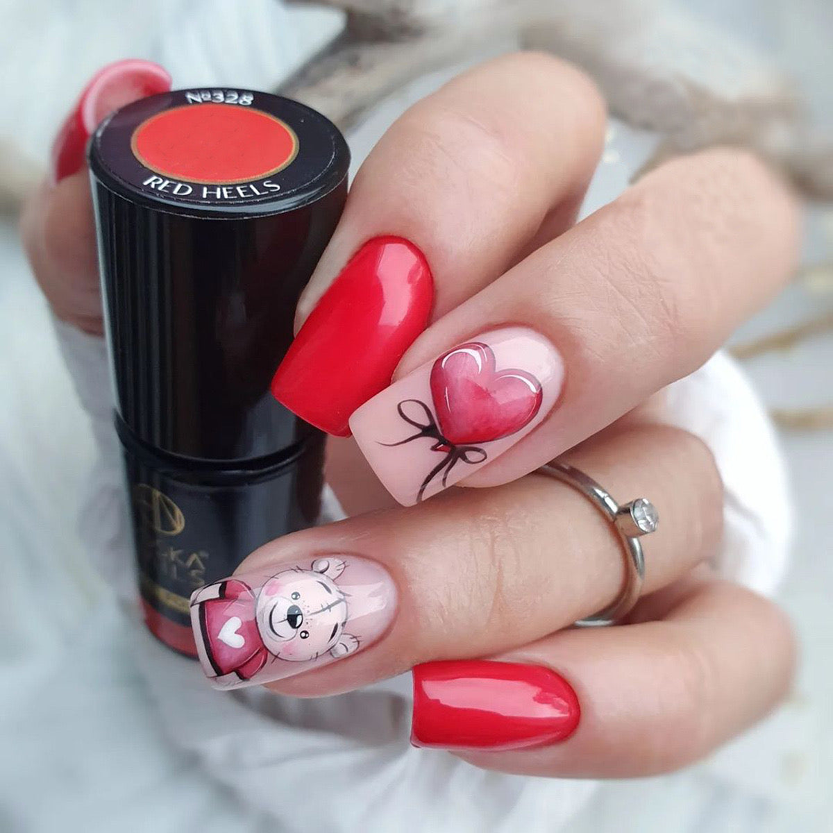 Nail polish with red and pink heart designs on nails, held by a hand.