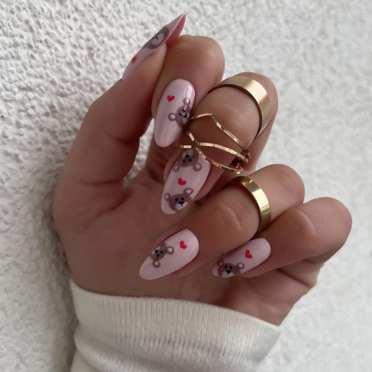 Hand with pink nail art featuring teddy bears and hearts on a white background