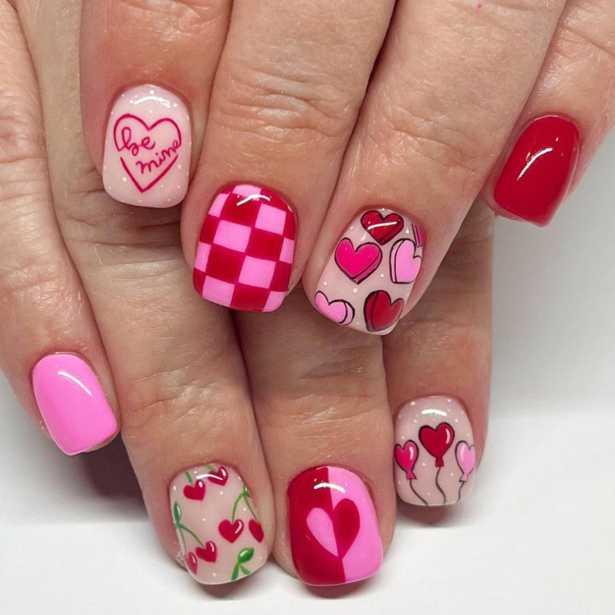 A set of short square and round press-on nails in pink, red, and white, featuring checkered patterns and heart motifs.