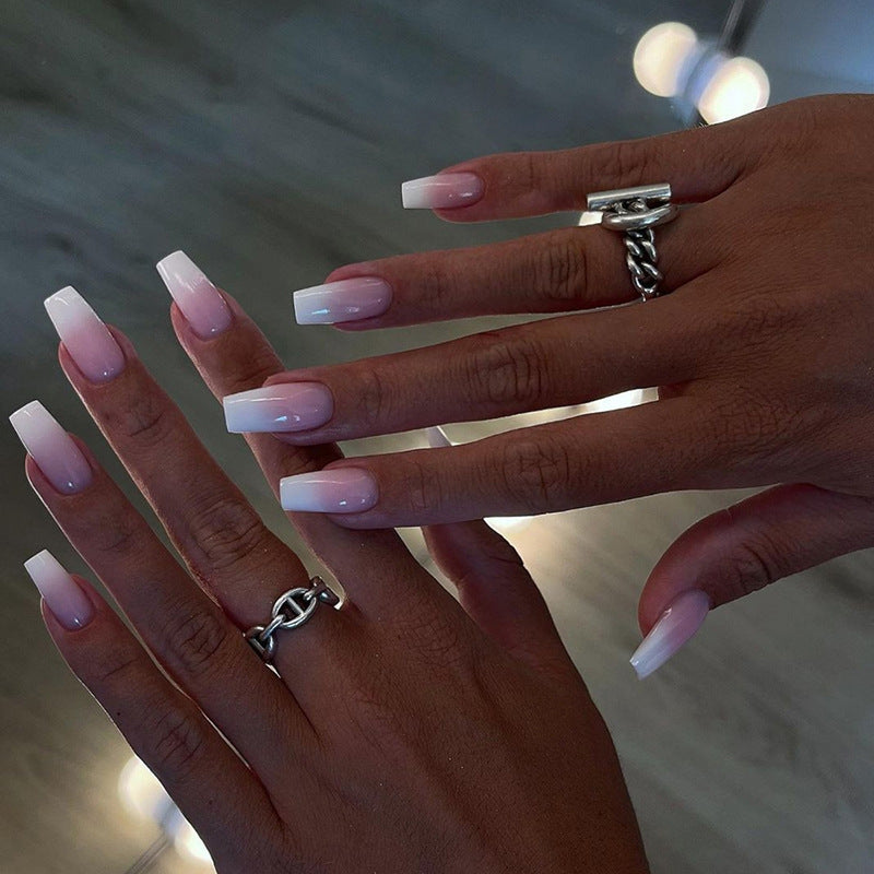 A pair of hands showcasing press-on nails with a medium coffin shape in a pink shade, accompanied by silver rings on the fingers.