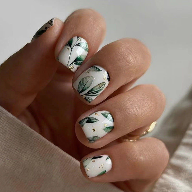 Nails with green leaf design on a neutral background