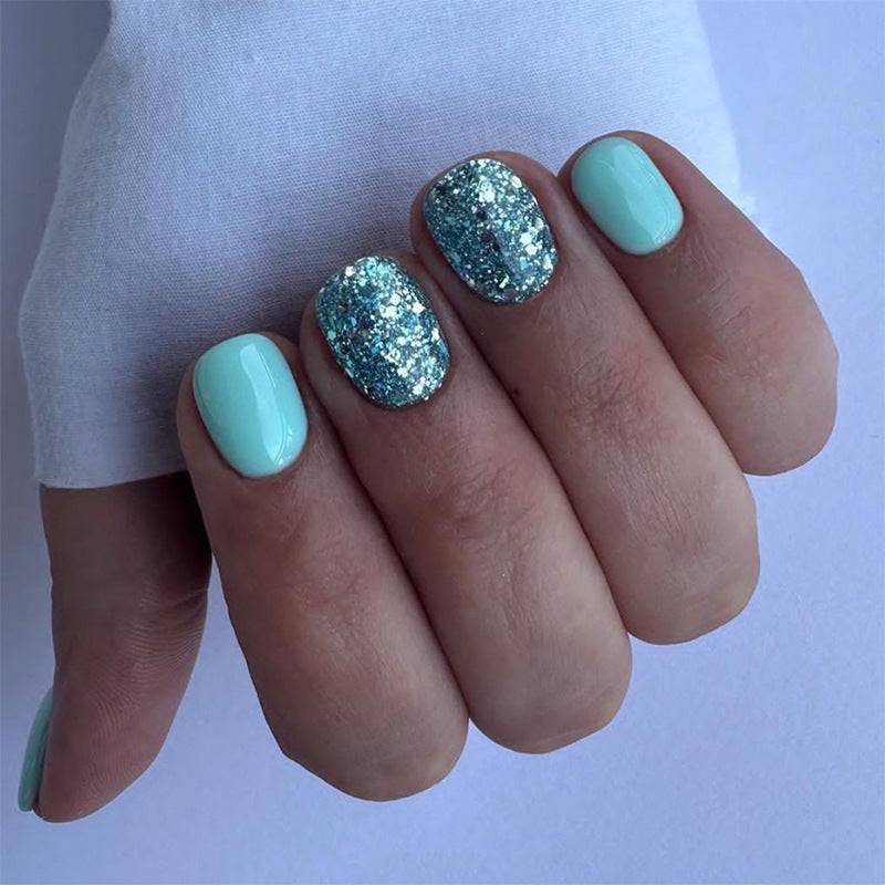 A hand with short squoval shaped nails with a glittery blue design on the tips.